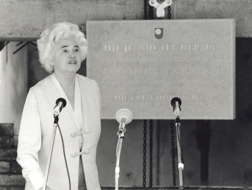 Baroness Lee of Asheridge, standing behind a microphone stand, with a foundation stone in the background.