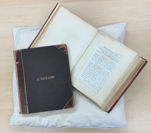 Photograph of the Sampson Low Collection, comprising two volumes of over 200 letters. There is a closed book with a black and brown 
leather cover entitled Autographs. This is overlapping with another volume that is open to display one of the letters.